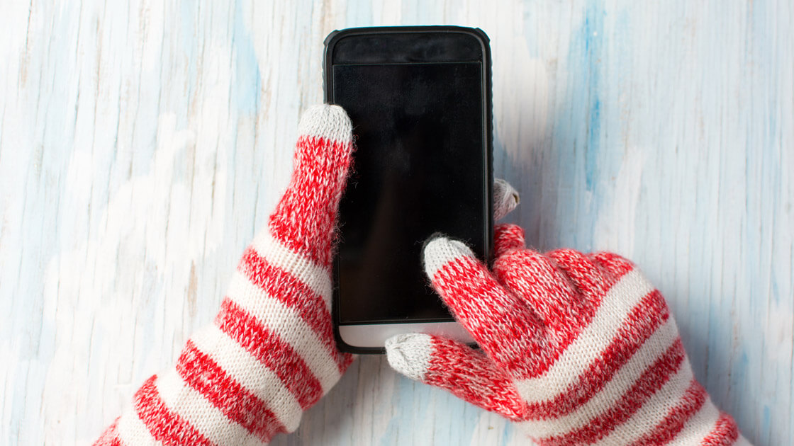 Hände mit Strickhandschuhen halten Handy